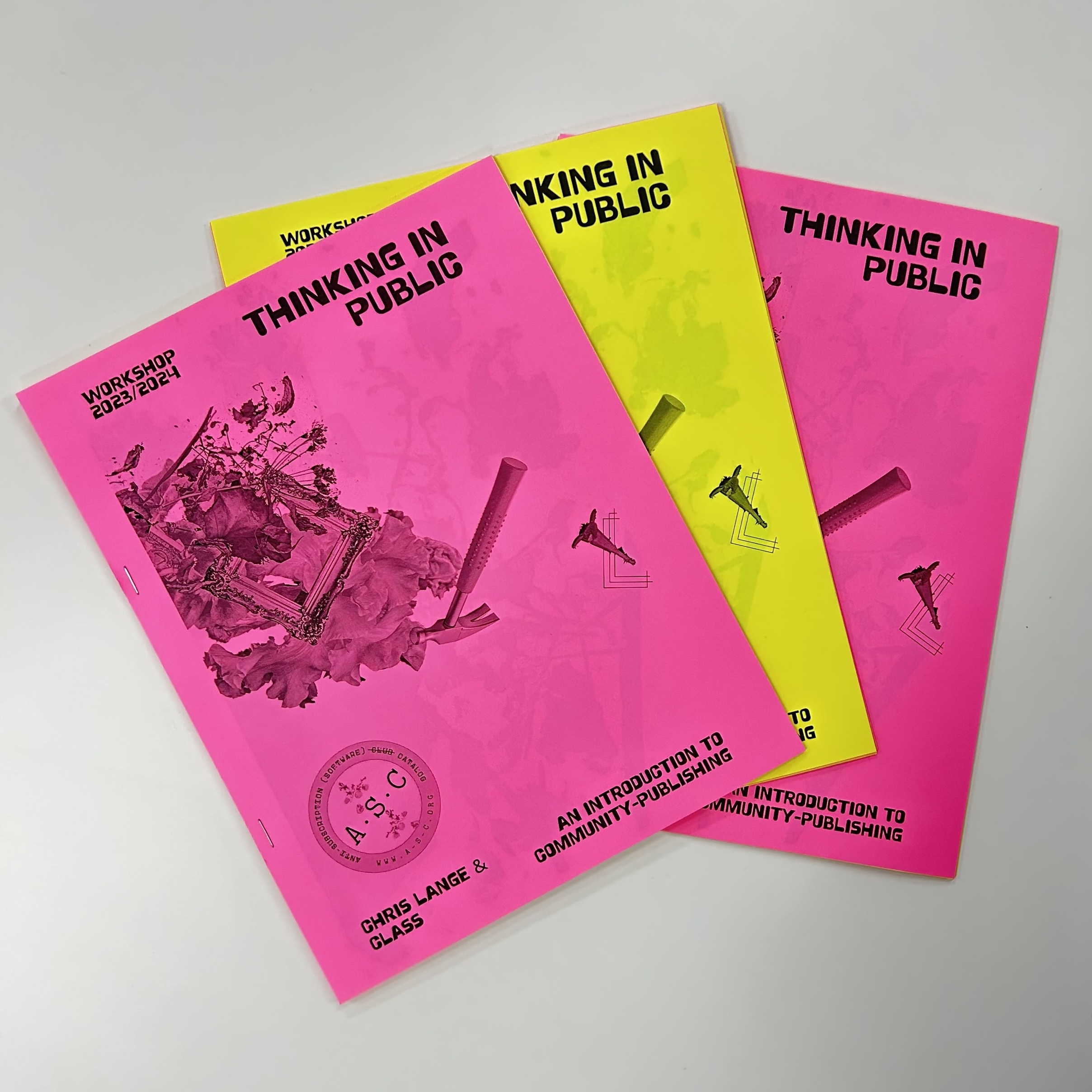 Three bright pink and yellow zine publication displayed on a table. 