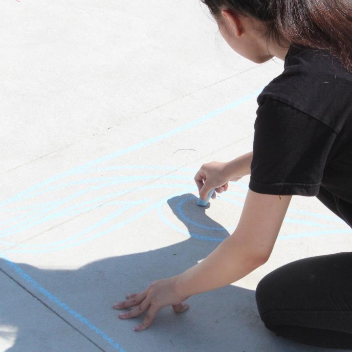 Student drawing with chalk on pavement