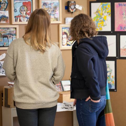 Two women stand in front of artwork at gallery.