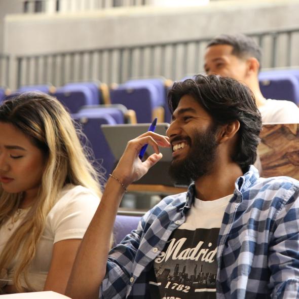 Smiling students sit in a lecture hall. 